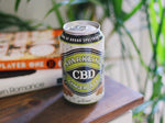 Can of CBD ginger ale on wooden indoor table beside plant and several books