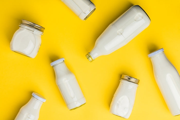 Seven milk bottles laying in varied positions on bright yellow surface