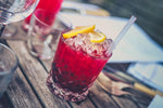 Red iced cocktails with lemon wedge garnishes on wooden picnic table