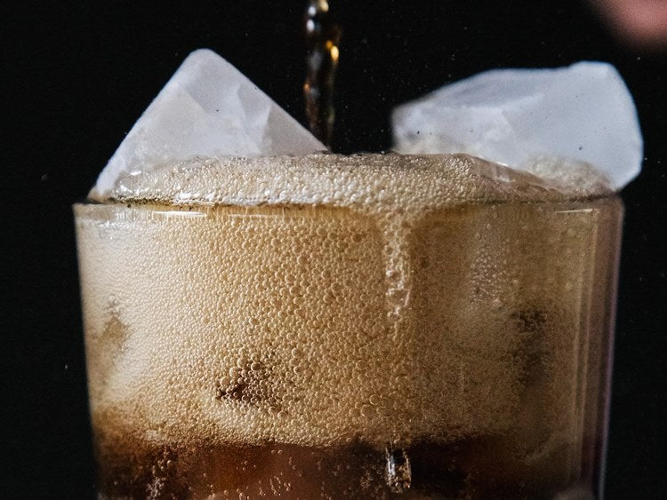 Close-up view of fizzing cola and ice at top of glass against black background