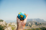 Hand holding miniature globe toward mountainscape