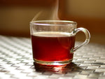 Steaming hibiscus tea in glass teacup on brown, woven wicker surface