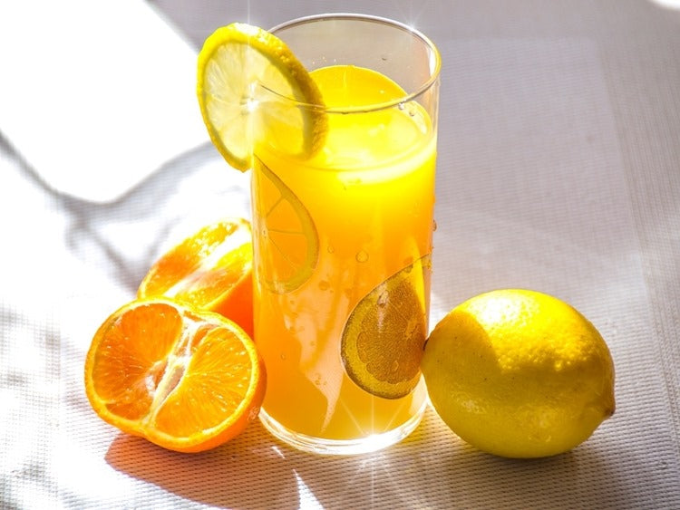 Glass of homemade lemonade with lemon slice garnish beside citrus fruits