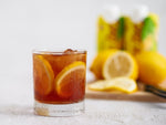 Frosty glass of iced tea with lemon slices on white table with lemons in background