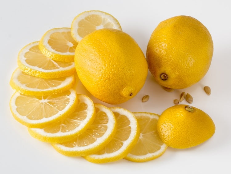 Two lemons beside ten slices and lemon seeds on flat white surface
