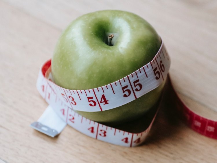 Cloth measuring tape wrapped around green apple on light wooden table