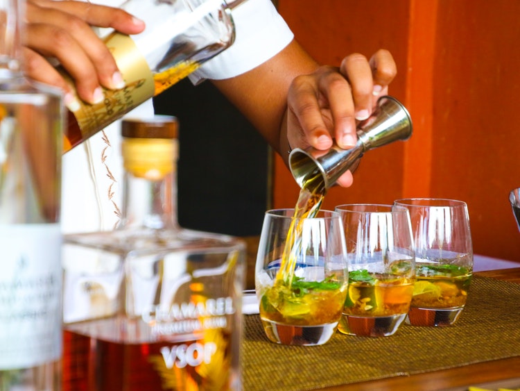 Bartended blending three cocktails fruity cocktails at wooden bar beside whiskey bottle