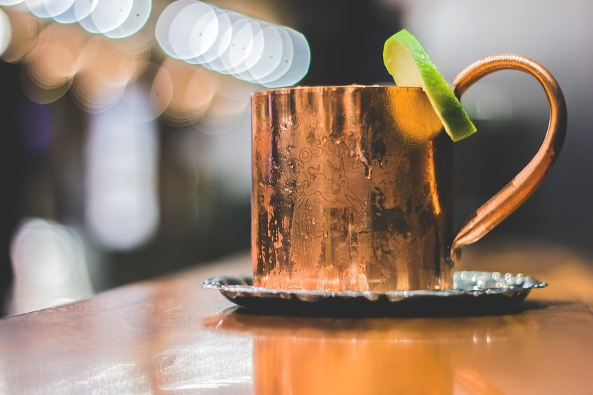 Moscow Mule drink with lime slice in copper mug on wooden bar countertop