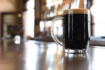 Tall glass stein of porter beer on surface of wooden bar
