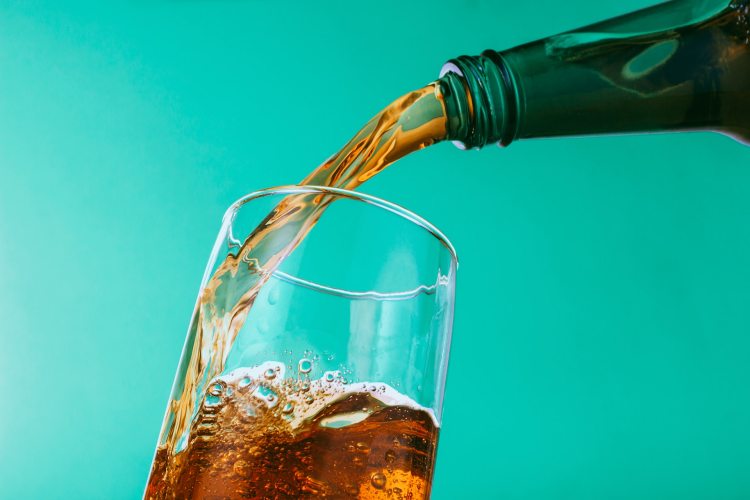 Soda pouring from green glass bottle into pint glass