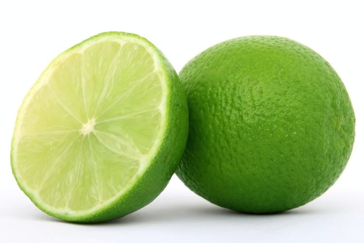 Sliced lime wedge beside whole lime white background