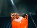Butane torch blazing lime wedge garnish on CBD cocktail with ice