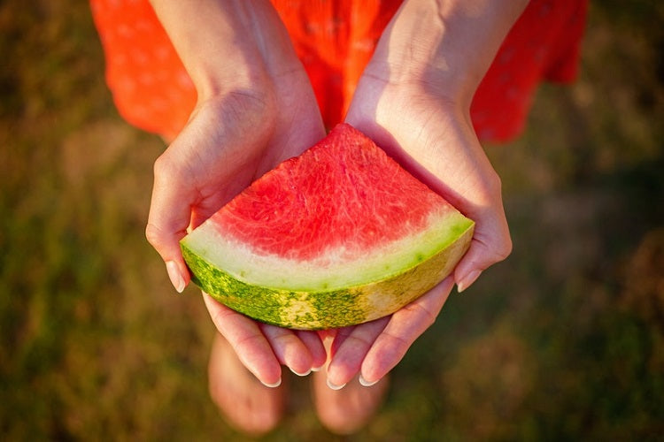 Hands holding watermelon slice outdoors above grassy area