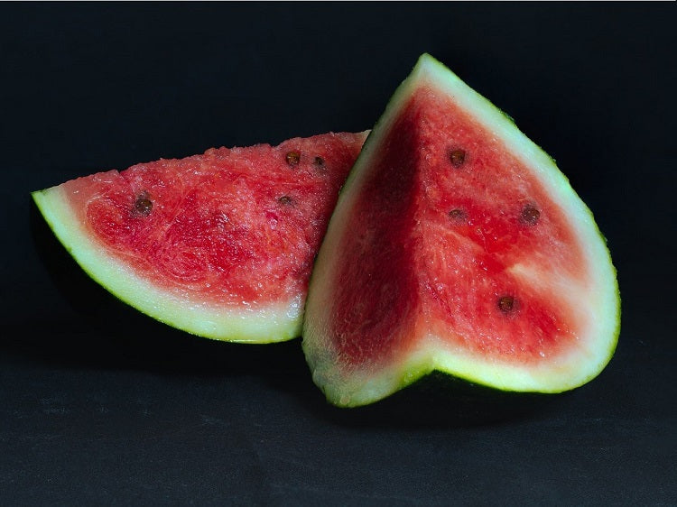 Two large watermelon wedges with black seeds on flat black surface